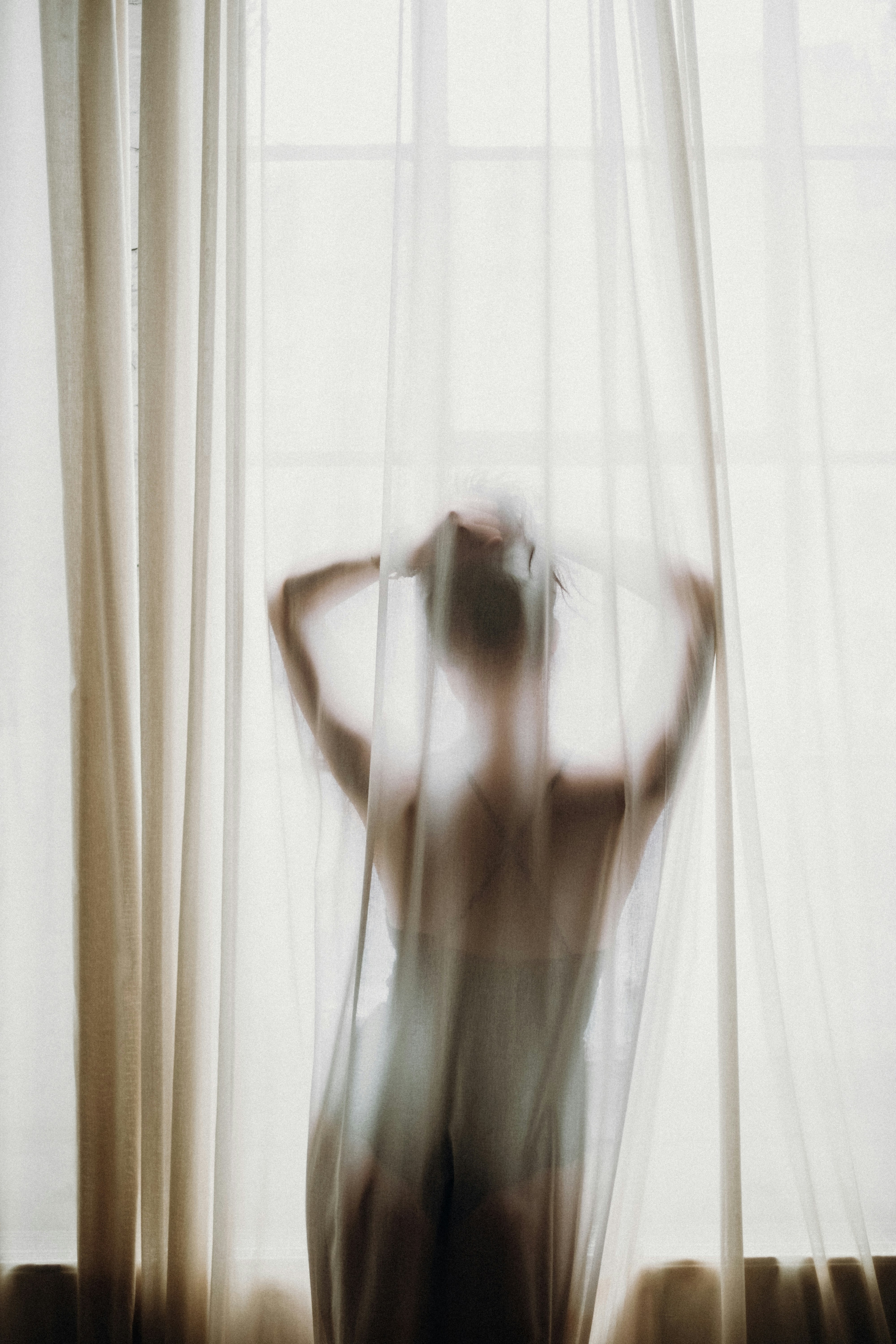 A woman standing behind a sheer curtain, evoking gentle, whole-body hormonal wellbeing